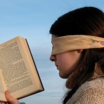 mlada žena s povezom preko očiju drži otvorenu knjigu
